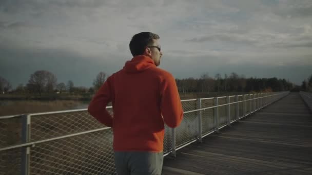 Мужчина Оранжевой Толстовке Бежит Через Национальный Парк Через Деревянный Мост — стоковое видео