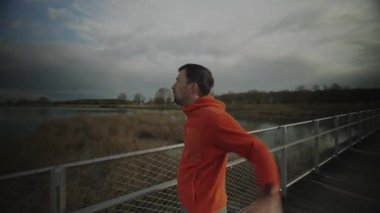 Kros koşucusu, soğuk sonbahar havasında ulusal parktaki ahşap köprüde antrenman yapmadan önce ısınıyor ve kaslarını esnetiyor. Düşük hava koşullarında koşmak ve antrenmandan önce ısınmak.. 