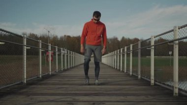 Sporcu açık hava kardiyo çalışmasından önce ısınıyor. Bir koşucu soğuk sonbahar havasında tahta bir köprüde koşmak için kaslarını ısıtır. Sağlıklı bir yaşam tarzı. Kırsal kesim. İz çalışmaları. 