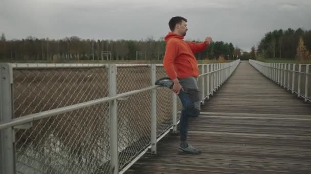 运动员在户外运动前热身 在寒冷的秋天里 一名慢跑者在一座木桥上慢跑 锻炼他的肌肉 以便在大自然中慢跑 健康的生活方式乡村跑步 小径跑动 — 图库视频影像