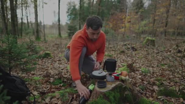 徒步旅行者将水从瓶中倒入锅中 放在木柴树桩上的煤气炉上 制成茶和升华的旅游食品 在森林里的篝火上烧水 背包露营炉系统 — 图库视频影像