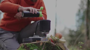 Gezgin, ormandaki bir kütüğe entegre bir pişirme sistemine su atıyor. Bir adam ıssız bir yerde gaz ocağında su kaynatacak. Sırt çantalı soba. Taşra yemekleri.. 