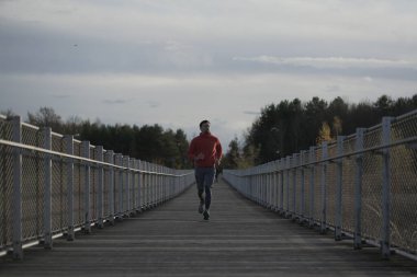 Doğada soğuk sonbahar havasında koşmak. Ulusal parktaki ahşap köprüden bir adam geçiyor. Kros antrenmanında bir sporcu. Kanada 'da egzersiz. Açık havada spor ve spor. Sağlıklı yaşam tarzı