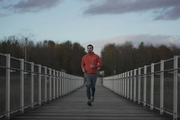 Running in cold fall weather in nature. A man runs across wooden bridge in national park. An athlete in cross country training. Workout in Canada. Active sport and fitness outdoors. Healthy lifestyle