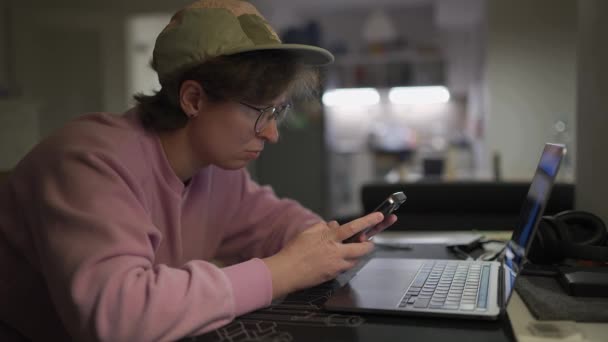 Egy Sapkában Szemüvegben Rózsaszín Pulóverben Egy Laptop Mögött Este Okostelefont — Stock videók