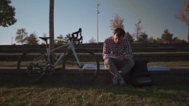 Öğrenci bisiklete bindikten sonra kampüs bahçesinde ödevini yapar. Bisikletçi parktaki bir çizim defterine not alıyor. - Açık havada öğreniyorum. Sağlıklı aktif yaşam tarzı. Dışarıda çalışan serbest çalışan.. 