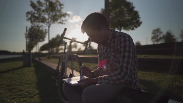 骑自行车锻炼后 大学生在大学校园的公园里做家庭作业笔记 骑自行车的人在笔记本上记笔记 在户外学习 健康积极的生活方式 — 图库视频影像