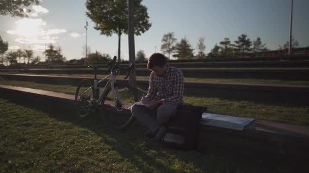 骑自行车后 学生们在校园花园做作业 自行车手在公园的素描本上做笔记 在户外学习 健康积极的生活方式 在外面工作的自由职业者 — 图库视频影像