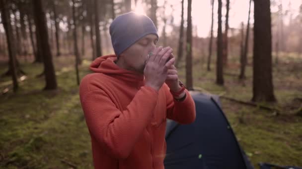 バックパッキング 屋外活動 テントの前でキャンプをしながら 秋の森の中でカップから暖かい飲み物を飲む旅行者 冷たい温度でお茶を飲みながら — ストック動画