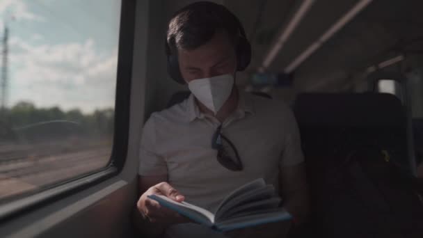 ワイヤレスヘッドフォンと読書本で夏にドイツの列車に旅行旅客 学生は電車に乗りながら無線電話で勉強書を読みます 大学への毎日の通勤 — ストック動画