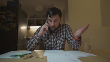 Adam, akşam yemek faturasını aldıktan sonra telefonda tartışıyor mutfakta masada oturuyor. Telefonda küfreden bir erkek banka makbuzuna bakıyor vergileri hesaplıyor, fatura dökümanını inceliyor.. 