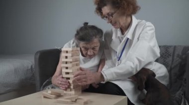 Hayvan terapisi, bunama ve Alzheimer hastalığından muzdarip yaşlıların bakımı. Kıdemli kadın ve doktor motor becerileri ve beyin egzersizleri yapıyorlar. Emeklilik merkezinde tahta blok kullanıyorlar.. 