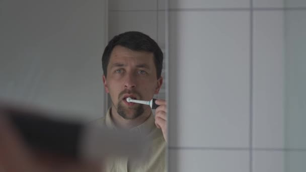 Beyaz Adam Dişlerini Banyoda Elektrikli Diş Fırçasıyla Fırçalar Aynadaki Yansımayı — Stok video