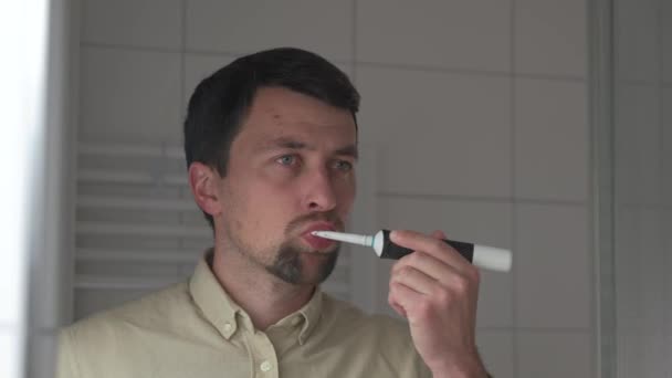 Кавказький Чоловік Чистить Зуби Електричною Зубною Щіткою Ванній Кімнаті Дивлячись — стокове відео