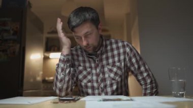 Finansal sorunlar. Mutfakta vergilere ve borçlara çözüm bulmaya çalışan üzgün bir adam. Para sorunlarını çözmek için beyin fırtınası yapmak. Stresli erkek maliyetleri hesaplar, tasarrufta para tutmaya çalışır.. 