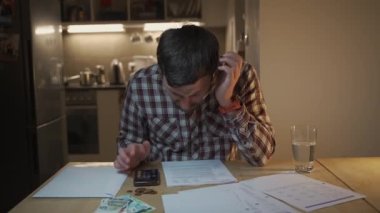 Finansal sorunlar. Mutfakta vergilere ve borçlara çözüm bulmaya çalışan üzgün bir adam. Para sorunlarını çözmek için beyin fırtınası yapmak. Stresli erkek maliyetleri hesaplar, tasarrufta para tutmaya çalışır.. 