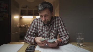 Mutfak dairesinde faturalara bakıp hesap makinesinde para hesaplayan sinirli bir adam. Depresyondaki erkek finans kontrolü. Nakit sorunları. Faturalar ve vergi harcamaları sayılıyor. Kamu hizmeti faturası. 