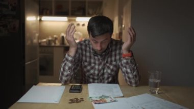 Mutfak dairesinde faturalara bakıp hesap makinesinde para hesaplayan sinirli bir adam. Depresyondaki erkek finans kontrolü. Nakit sorunları. Faturalar ve vergi harcamaları sayılıyor. Kamu hizmeti faturası. 