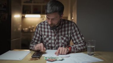 Finansal sorunlar. Mutfakta vergilere ve borçlara çözüm bulmaya çalışan üzgün bir adam. Para sorunlarını çözmek için beyin fırtınası yapmak. Stresli erkek maliyetleri hesaplar, tasarrufta para tutmaya çalışır.. 