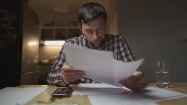 Finansal sorunlar. Mutfakta vergilere ve borçlara çözüm bulmaya çalışan üzgün bir adam. Para sorunlarını çözmek için beyin fırtınası yapmak. Stresli erkek maliyetleri hesaplar, tasarrufta para tutmaya çalışır.. 