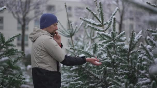 Muž Vybere Vánoční Stromeček Venkovním Trhu Sněhu Mluví Telefonu Manželkou — Stock video