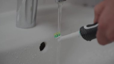 Erkekler dişlerini fırçaladıktan sonra elektrikli diş fırçasını lavaboda suyun altında tutarlar. Erkek, ses enerjili diş fırçasını musluk suyuyla yıkıyor. Sabah ağız temizliği.. 