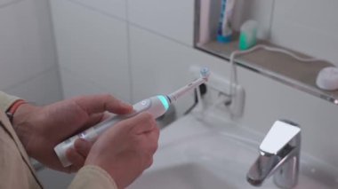 Elektrikli diş fırçası tutan adam. Akıllı elektrikli diş fırçası. Sağlık için modern teknoloji. Sağlıklı dişler. Diş hekimliği. Erkek eller beyaz güç diş fırçasını açıp kapayarak değiştiriyor. Ağız temizleme aracı. 