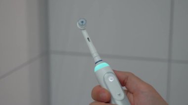 Erkek elinin beyazlı ultrasonik diş fırçasını açıp kapayarak banyonun arka planında mavi bir arka ışık oluşturduğu yakın plan. Ağız bakımı ve beyaz dişler. Elektrikli diş fırçası. Diş temizleyici güç aracı. 
