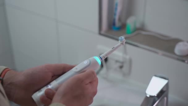 バスルームの背景に青色の光と音の白い歯ブラシをオンまたはオフにマンの手 歯科衛生と歯のきれいな白 電気歯ブラシ 口を掃除するためのパワーツール — ストック動画