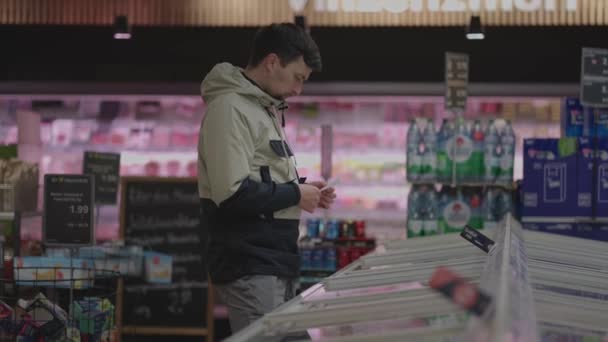 Мужчина Покупатель Тщательно Выбирает Замороженные Продукты Морозильной Камере Супермаркете Зимой — стоковое видео