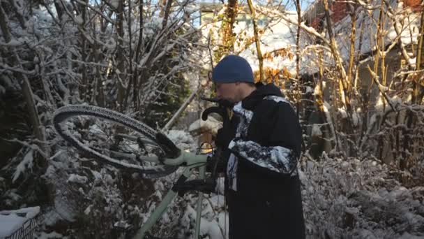 冬天的时候 骑自行车的人在后院刷自行车 然后把它拿到停车场 冬季自行车和自行车清洁 男人在屋外擦自行车轮子上的雪 — 图库视频影像