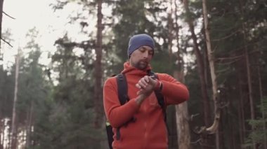 Sırt çantası sonbahar ormanlarındaki bir spor saatinde yön ve rotayı kontrol eder. Yürüyüşçü bir gezide saate bakıyor. Yürüyüş yolunda akıllı saat, pusula ve kalp atış hızı. Teknoloji ve seyahat. 