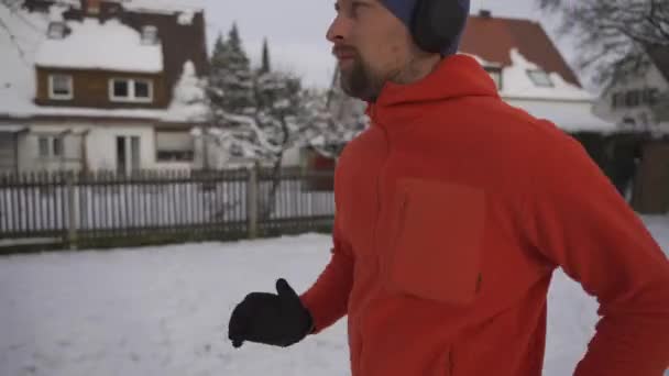 都市の公園を通って雪の道をジョギングする男は ドイツの冬にイヤホンで音楽を聴く 冷たい天候の中でヘッドフォンを着用して作業をアスレチックマン 冬は雪の中を走る — ストック動画