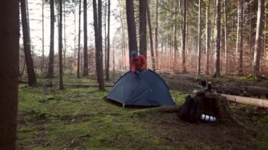 Camping, tourism and travel concept. Man setting up tent outdoors. Hiker assembles campsite tent in the autumnal forest. Traveler installing tent in autumn woods. Outdoor weekend Activity. 