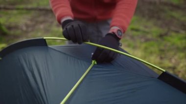 Man hiker sets up camping tent in the fall forest on backpacking expedition. Traveler setting an overnight tent in the wilderness in the fall. Theme of tourism and trekking. Outdoor weekend activity. 