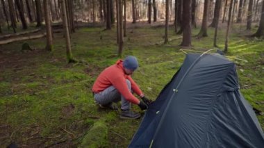 Camping, tourism and travel concept. Man setting up tent outdoors. Hiker assembles campsite tent in the autumnal forest. Traveler installing tent in autumn woods. Outdoor weekend Activity. 