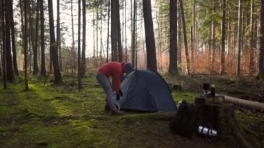 Camping, tourism and travel concept. Man setting up tent outdoors. Hiker assembles campsite tent in the autumnal forest. Traveler installing tent in autumn woods. Outdoor weekend Activity. 