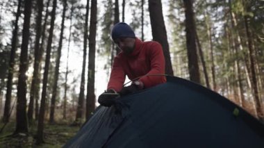 Man hiker sets up camping tent in the fall forest on backpacking expedition. Traveler setting an overnight tent in the wilderness in the fall. Theme of tourism and trekking. Outdoor weekend activity. 