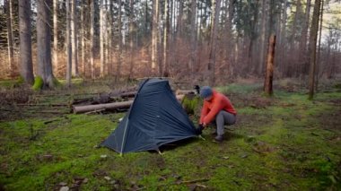 Man hiker sets up camping tent in the fall forest on backpacking expedition. Traveler setting an overnight tent in the wilderness in the fall. Theme of tourism and trekking. Outdoor weekend activity. 
