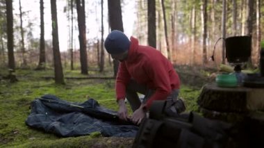 Tourist makes camp in woods, sets up tent in meadow in fall forest, prepares for an overnight stay in campsite. Backpacker builds tent on solo autumn trip in forest. Hiking and staying in nature. 