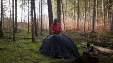 Man hiker sets up camping tent in the fall forest on backpacking expedition. Traveler setting an overnight tent in the wilderness in the fall. Theme of tourism and trekking. Outdoor weekend activity. 