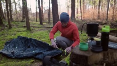 Man hiker sets up camping tent in the fall forest on backpacking expedition. Traveler setting an overnight tent in the wilderness in the fall. Theme of tourism and trekking. Outdoor weekend activity. 