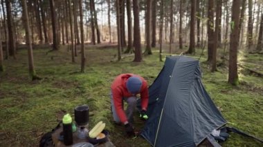 Camping, tourism and travel concept. Man setting up tent outdoors. Hiker assembles campsite tent in the autumnal forest. Traveler installing tent in autumn woods. Outdoor weekend Activity. 