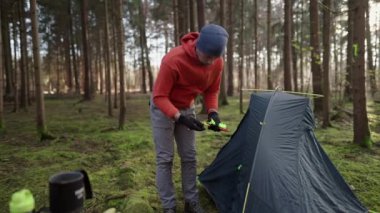 Tourist makes camp in woods, sets up tent in meadow in fall forest, prepares for an overnight stay in campsite. Backpacker builds tent on solo autumn trip in forest. Hiking and staying in nature. 