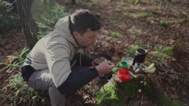 Wanderer eating fast cooking meals with water from gas stove in woods during autumn hike. Traveler eats freeze dried food when backpacking out of travel cookware. Trekker having oatmeal while hiking. 