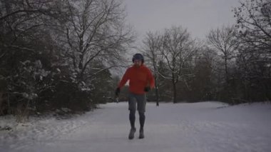 Male jogger running on a slippery snow surface in a park in winter in loose footwear in winter. Wrong sneakers for running in snowy weather. Workout safety. Training outside in cold snowy weather. 