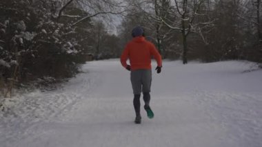 Wrong outfit and footwear for running on slippery surfaces in winter. Man jogging in snow cold weather and slips. Slippery sneakers with wrong soles for trail running on ice covered paths in woods. 