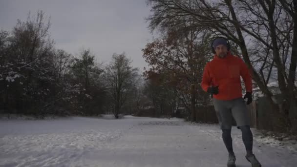 冬に滑りやすい表面を走るための間違った服や履物 男は雪の寒い天候とスリップでジョギング 靴底が悪い滑りやすいスニーカーで 木の氷で覆われた道を走るトレイル — ストック動画