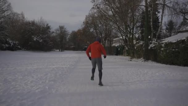 冬は緩んだ履物で冬の公園の滑りやすい雪の表面で走る男性のジョギング 雪の天気で走るための間違ったスニーカー 安全装置を使え 寒い雪の中外での訓練 — ストック動画