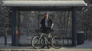 Bicyclist bicycle broke down in winter and he waits long time for bus at snowy stop after snowstorm in Germany. Male cyclist really frozen waiting for transport at standstill for long time in winter. 